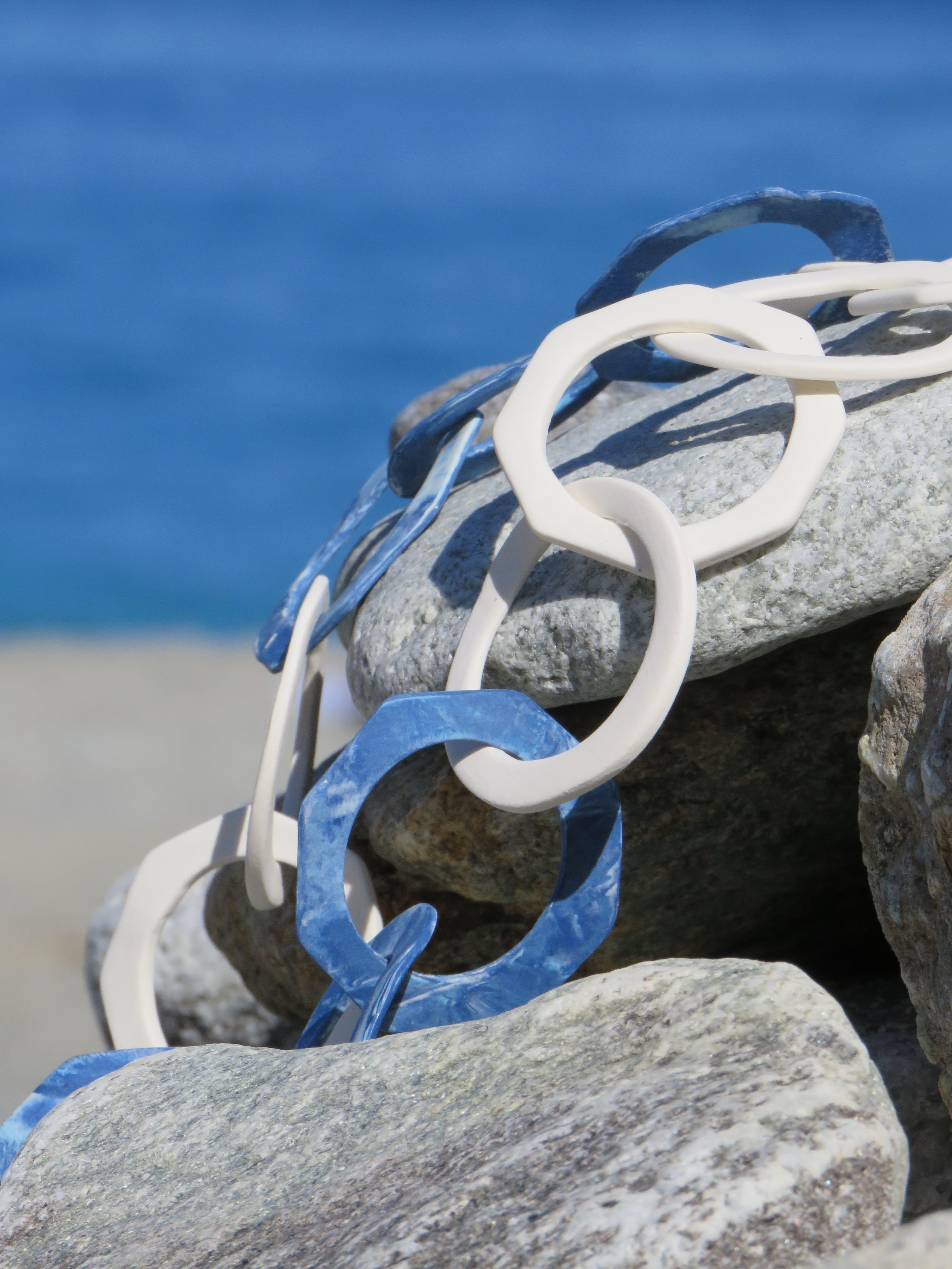Collana a maglie alternate cerchi ed esagoni in porcellana nerikomi bianco e blu, su sassi con mare calabrese sullo sfondo
