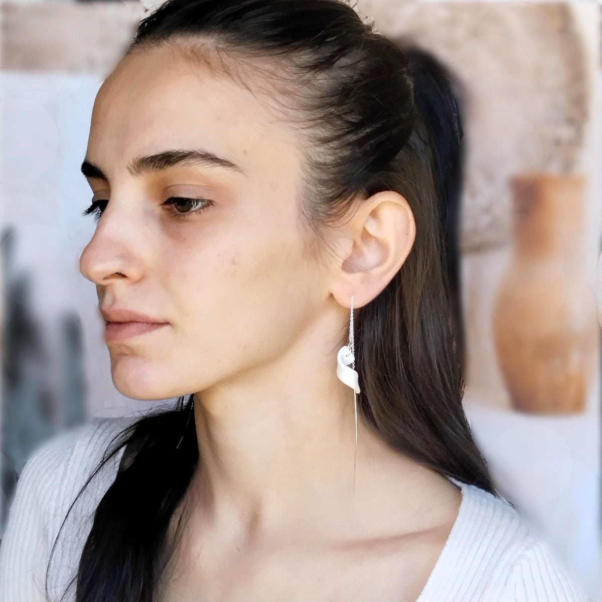 Orecchino Turbine Maviart indossato, porcellana bianca a spirale con inclusione in platino e catenella lunga in argento.