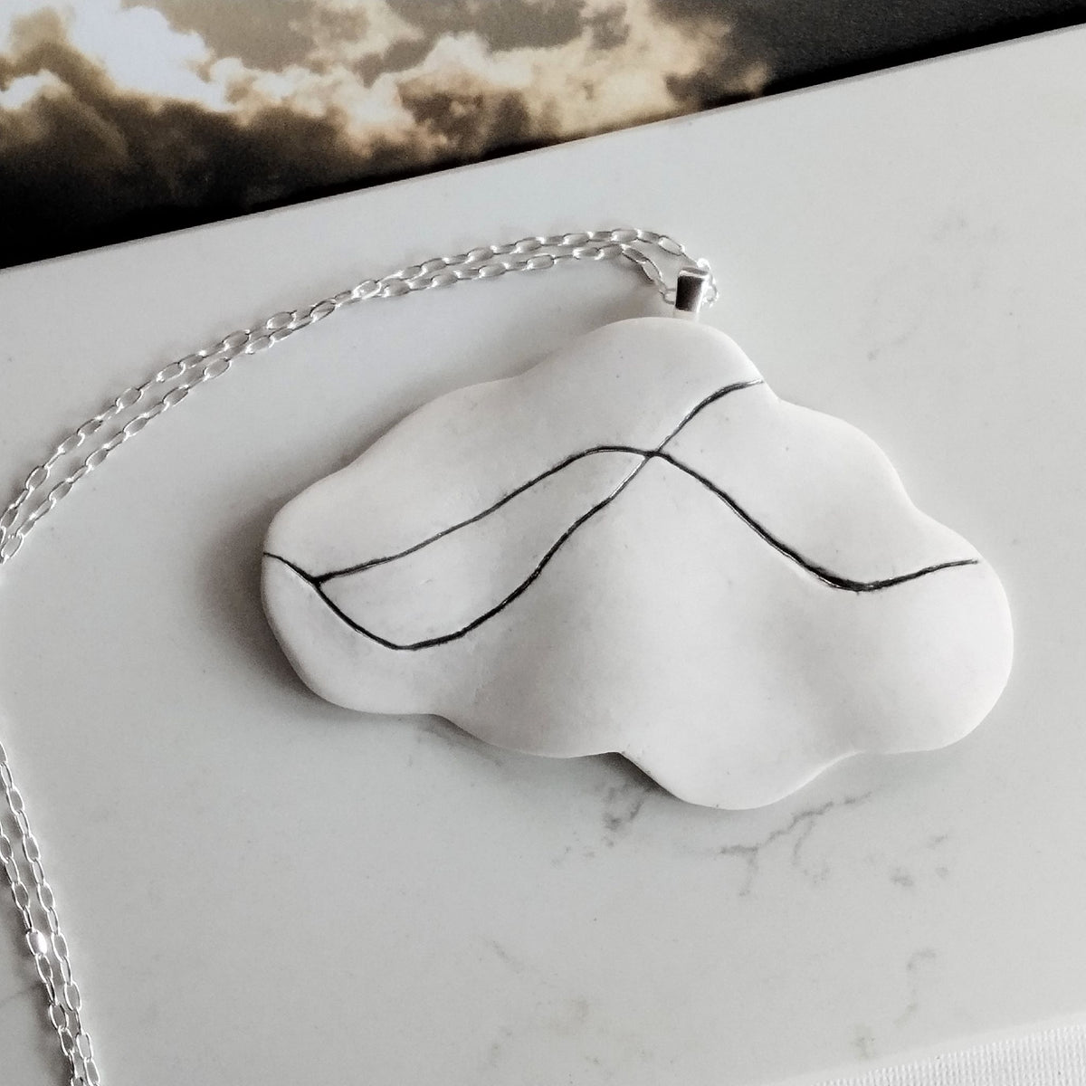 Collana Cumulo in posa dall’alto, con pendente in porcellana bianca attraversato da linee in platino e catena in argento.