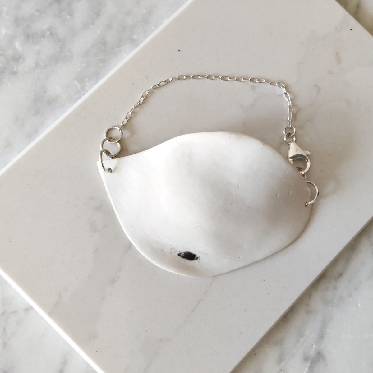 Bracciale Soffio Maviart in posa dall'alto: porcellana bianca e catena in argento sterling