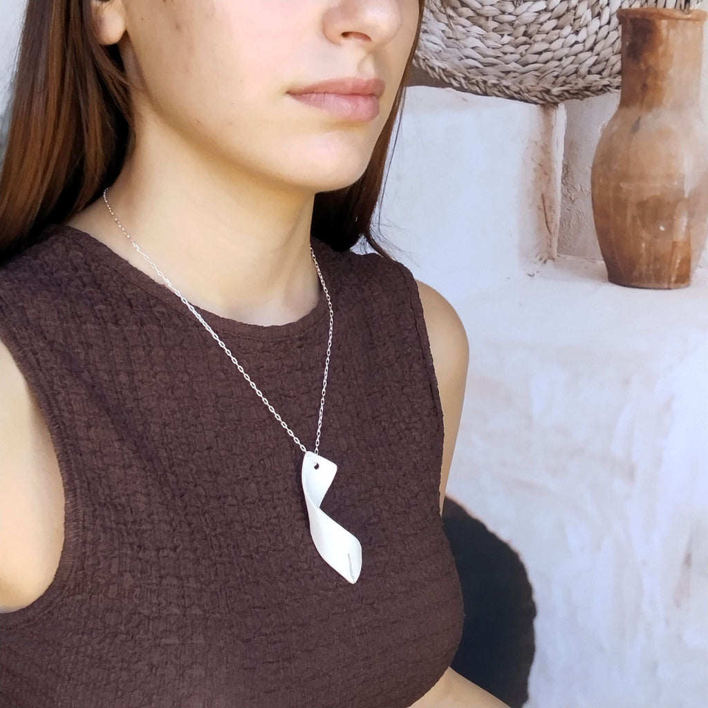 Collana Turbine indossata su un top scuro, con pendente in porcellana bianca e catena in argento.