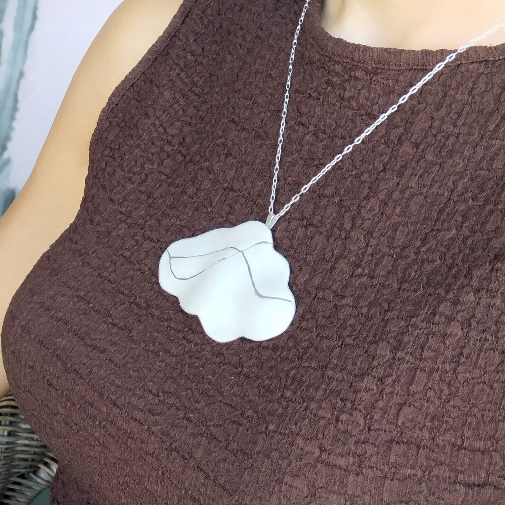 Primo piano del pendente Cumulo indossato, con profilo ondulato in porcellana bianca e inclusioni lineari di platino.